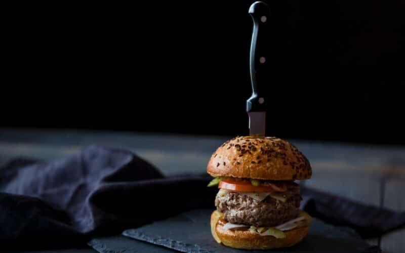 burger skewered with knife near black textile